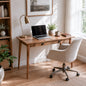 A rustic wooden writing desk with two drawers, styled in a bright home office with a laptop, brass desk lamp, potted plant, and a cream-colored swivel office chair.